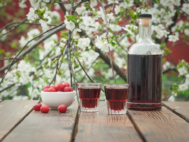 Uma garrafa e copos com licor de cereja e frutas vermelhas