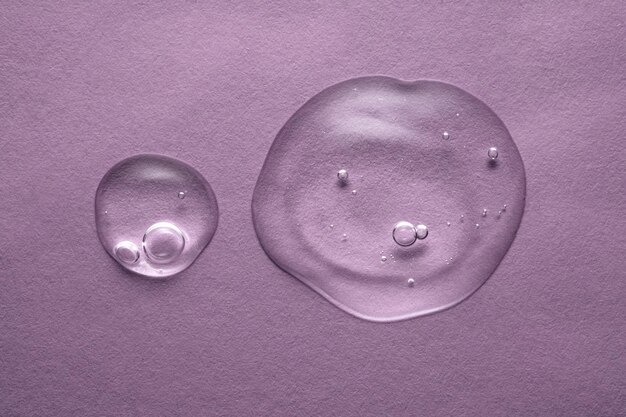 Uma gota de gel cosmético transparente sobre um fundo roxo