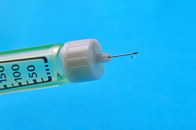 Uma gota de medicamento na extremidade de uma agulha de seringa com divisões de dosagem em close-up em um fundo azul vacinação da população