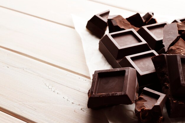 Uma grande barra de chocolate preto sobre um fundo branco de madeira com espaço para texto.