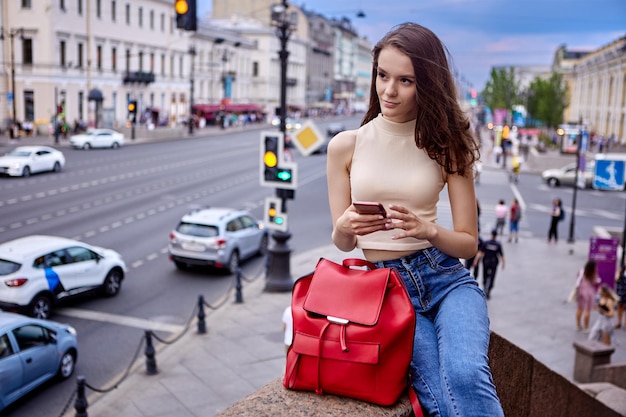 Uma grande bolsa de couro vermelha é segurada por uma aluna esguia de jeans e top caminhando em meio à multidão