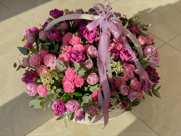 Uma grande cesta bonita de flores rosa brilhantes com tulipas, rosas e eucalipto. Imagem de fundo com flores sob a luz do sol