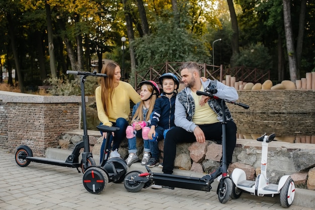 Uma grande família feliz anda de Segways e scooters elétricos no parque em um dia quente de outono durante o pôr do sol