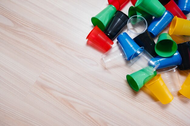 Uma grande pilha de copos de plástico multicoloridos espalhados pelo chão com espaço livre. Poluição do meio ambiente por dejetos humanos