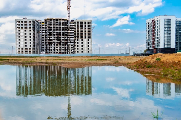 Uma grande poça após a chuva no canteiro de obras de uma grande instalação residencial Reflexão na água do canteiro de obras e guindastes contra o fundo do céu pôr do sol