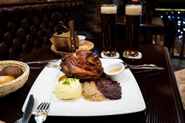 Uma grande porção de carne de porco grelhada e cerveja na mesa no pub Pernil de porco assado com chucrute e purê de batatas na mesa de madeira