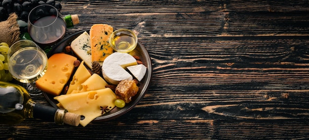 Uma grande variedade de queijos queijo brie gorgonzola queijo azul uvas mel nozes vinho tinto e branco em uma mesa de madeira Vista superior Espaço livre para texto