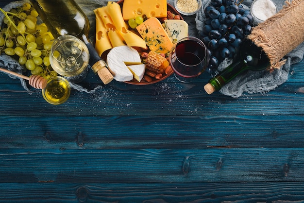 Uma grande variedade de queijos vinho mel nozes e especiarias em uma mesa de madeira azul Vista superior Espaço livre para texto
