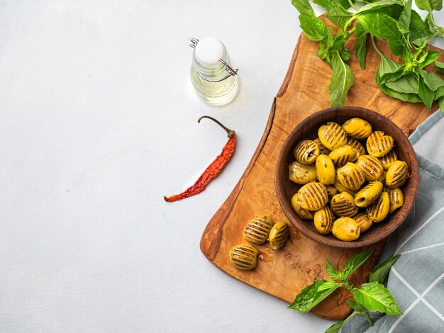 Uma grelha verde de azeitonas em uma tigela de madeira em um fundo claro com azeite de oliva e manjericão O conceito de lanches saudáveis vegetarianos Vista superior e espaço de cópia