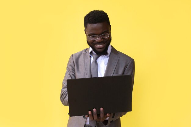 Uma imagem de feliz animado jovem africano isolado sobre uma parede amarela, usando o computador portátil.