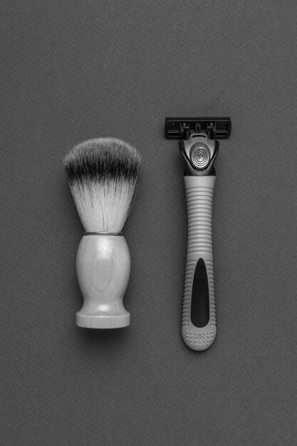 Uma imagem em preto e branco de uma escova de barbear e uma navalha de homem em um fundo cinza