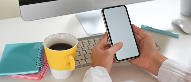 Uma imagem recortada de mãos está usando um celular com tela vazia na mesa de trabalho.