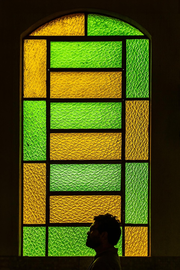 Foto uma janela com vidro colorido verde e amarelo em uma igreja com a silhueta de uma pessoa em backli