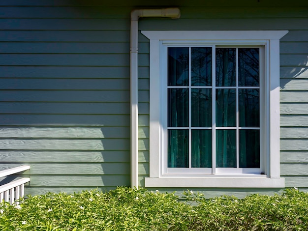 Uma janela de casa branca com decoração de cortina de vidro, verde no pequeno residente de madeira verde-claro com espaço de cópia, vista do exterior