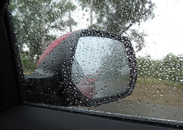 Uma janela lateral do carro encharcada de chuva dificulta a visão no espelho retrovisor