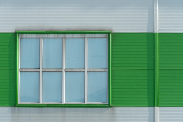 Uma janela na parede de uma fábrica moderna ou um grande centro comercial Detalhes da fachada de alumínio de um edifício industrial O edifício é feito de placas de alumínio corrugado de verde e branco