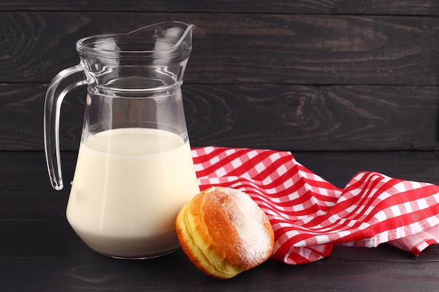 Uma jarra de leite e um donut, uma toalha de mesa em uma superfície escura