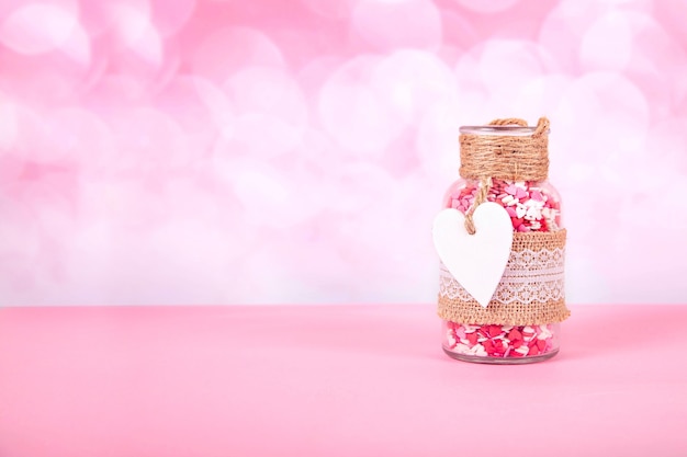 Uma jarra de vidro com corações coloridos em um fundo rosa com bokeh