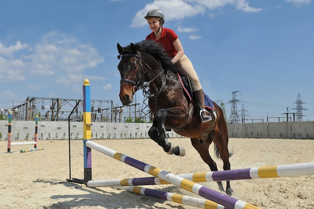 Uma jóquei cavalgando um cavalo pula uma barreira