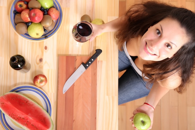 Uma jovem adulta com frutas e vinho na cozinha.