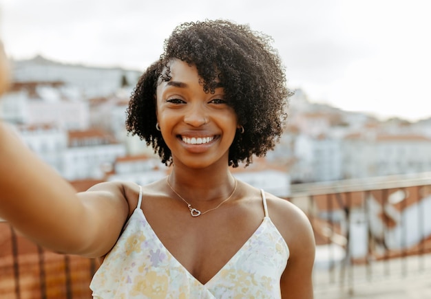 Uma jovem afro-americana sorridente caminha pela cidade e aproveita a viagem para fazer um vídeo ou selfie no telefone