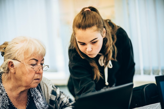 Uma jovem ajuda uma mulher mais velha na aula a trabalhar com um laptop