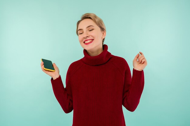 Uma jovem alegre com um suéter vermelho e um smartphone em um fundo azul