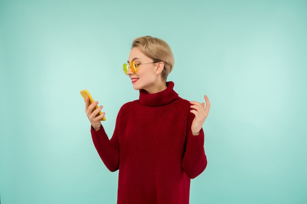 Uma jovem alegre com um suéter vermelho e um smartphone em um fundo azul