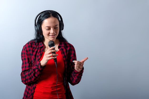 Uma jovem alegre em roupas casuais com fones de ouvido canta música no microfone simulando o espaço da cópia