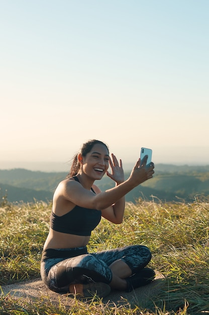 Foto uma jovem alegre em roupas esportivas, tendo um bate-papo por vídeo ao ar livre, sorrindo e acenando