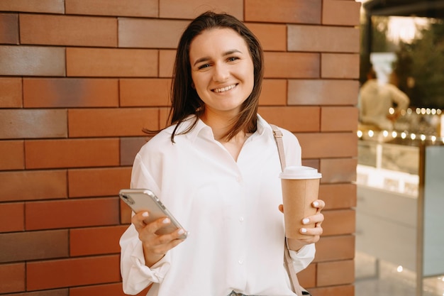 Uma jovem alegre está usando o telefone enquanto desfruta de seu café ao ar livre