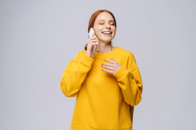 Uma jovem alegre vestindo um elegante suéter amarelo falando por telefone celular em fundo branco isolado