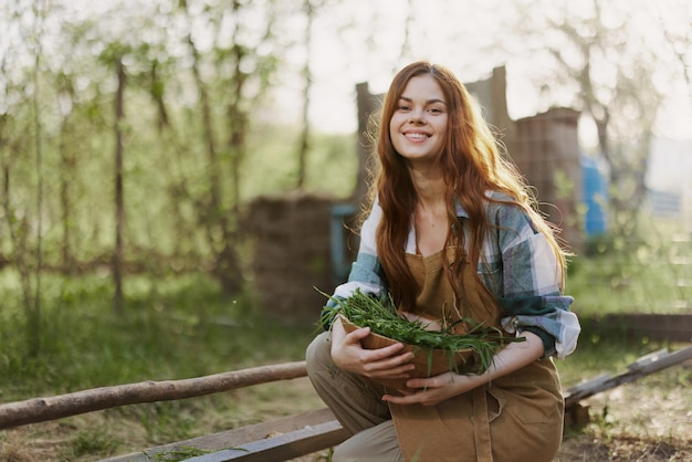 Uma jovem alimenta suas galinhas na fazenda com grama vestindo uma simples camisa a quadros calças e avental e sorrindo para a câmera cuidando dos animais foto de alta qualidade