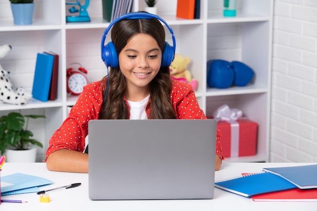 Uma jovem aluna com fones de ouvido sem fio sentada à mesa usando laptop