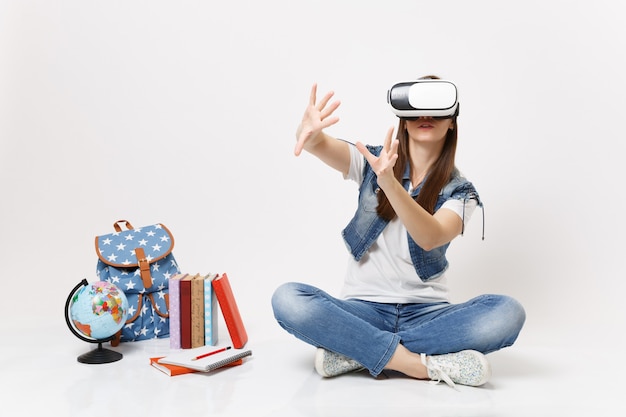 Uma jovem aluna com óculos de realidade virtual toca algo como apertar o botão, apontando para uma tela virtual flutuante perto do globo, mochila, livro escolar isolado