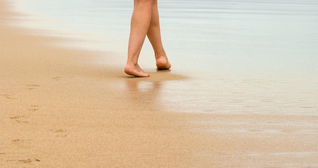 Uma jovem andando descalça na areia deixando pegadas na praia dourada Viagens de férias e conceito de liberdade