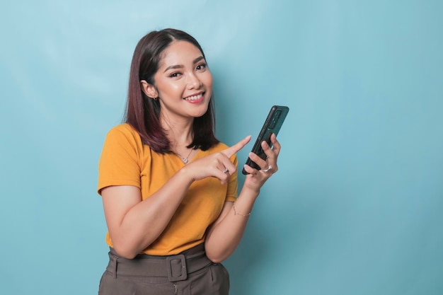 Uma jovem animada apontando seu smartphone na mão isolada em fundo azul