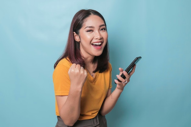 Uma jovem animada está sorrindo enquanto segura seu smartphone na mão isolado em fundo azul