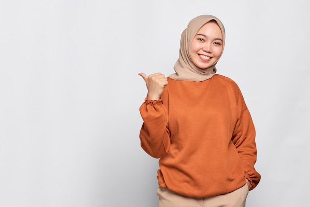 Uma jovem asiática alegre de camisa laranja apontando dedos para o espaço de cópia isolado sobre fundo branco