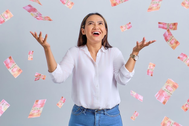 Uma jovem asiática alegre regozijando-se com o sucesso com notas de dinheiro voando no ar isoladas sobre fundo branco