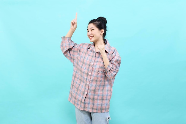 Uma jovem asiática apontando olhando para anúncios vestindo uma camisa xadrez em pé e se sentindo feliz e confiante em fundo azul