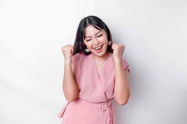 Uma jovem asiática com uma expressão feliz e bem-sucedida usando blusa rosa isolada por fundo branco