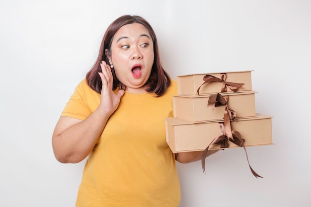 Uma jovem asiática de tamanho grande chocada está vestindo camisa amarela e segurando caixas de presentes e sacolas de compras