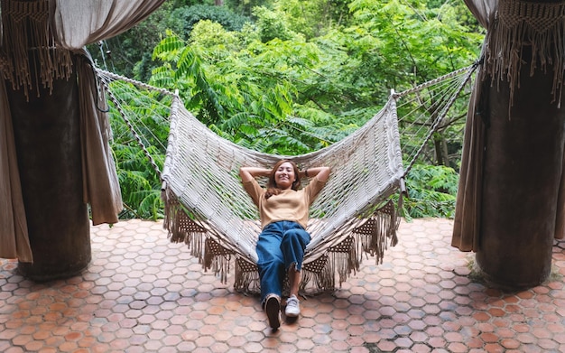 Uma jovem asiática deitada e relaxando na rede com natureza verde ao fundo