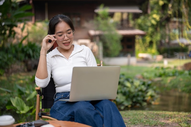 Uma jovem asiática está trabalhando remotamente em seu quintal ou em um café ao ar livre usando seu laptop