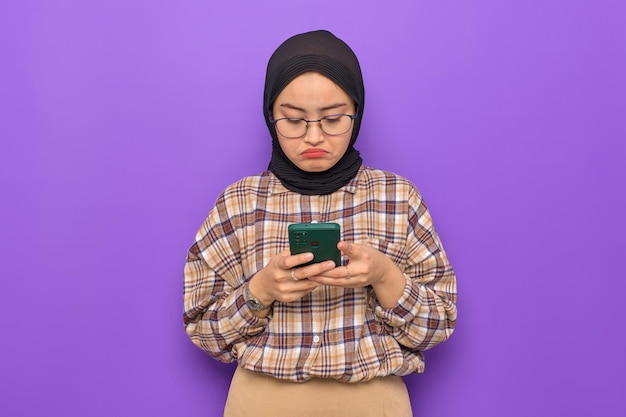 Uma jovem asiática irritada em camisa xadrez usando telefone celular recebeu más notícias isoladas em fundo roxo