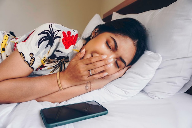 Uma jovem asiática na cama sente sono, ela está deitada de lado e bocejando
