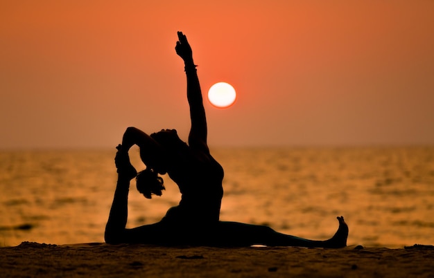 Foto uma jovem asiática saudável posando para praticar ioga de ave do paraíso na praia de pedra com céu azul nublado