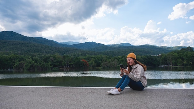 Uma jovem asiática segurando e usando telefone celular enquanto viajava montanhas e lago