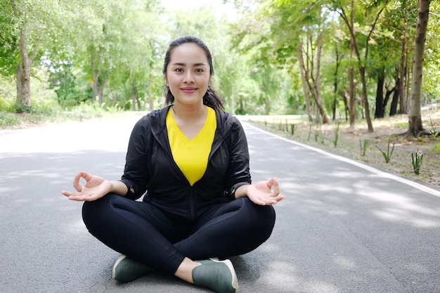 Uma jovem asiática sorridente em roupas esportivas sentada e fazendo ioga para meditação no jardim natural